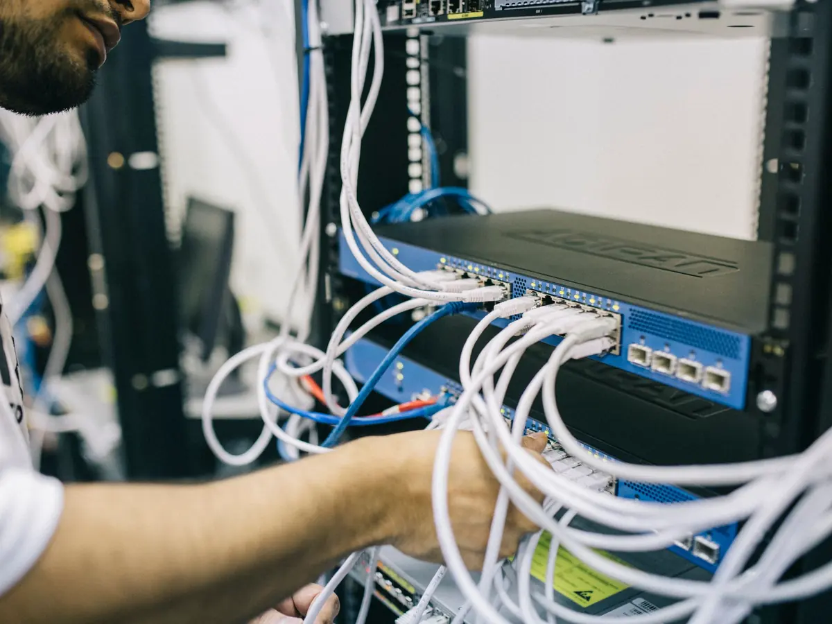 Técnico organizando cabos de rede estruturada em rack com switch